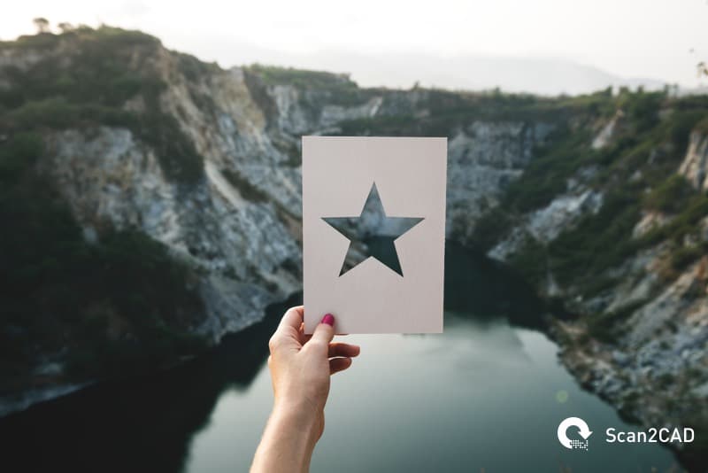 CNC cut paper design held in front of mountains and river